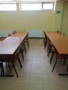 wnętrze klasy. w dwóch rzędach ustawione ławki szkolne z krzesłami
