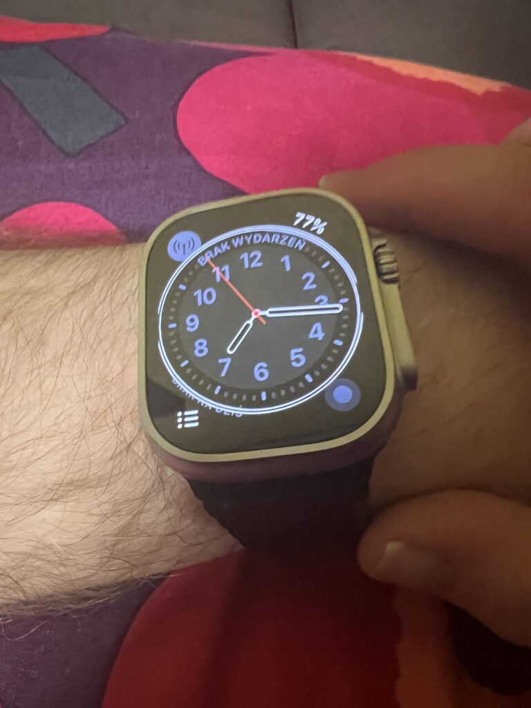 Apple Watch Ultra z czarną, stalową bransoletą panelową. Na ekranie tarcza Kalifornia. Zegarek zapięty na nadgarstku.