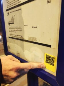 Palec wskazujący na naklejkę z kodem QR i opisem brajlowskim na rozkładzie jazdy. fot. Agnieszka Majnusz
