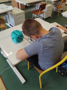 Uczeń, korzystający z pomocy naukowej, na biurku duża, niebieska kostka do gry