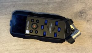Rejestrator Zoom H6essential z góry. Pokazany jest ekran, przyciski sterujące nagrywaniem, cztery przyciski wyboru kanałów oraz podłączony mikrofon stereo.